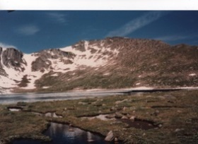 My-photo-taken-on-top-of-one-of-the-Rocky-mountains--and-there-is-a-shallow-body-of-cold-crystal-clear-water--and-green-plant-life-can-be-seen-under-the-surface-and-in-the-background-are-the-tips-of-the-mountains--and-while-they-have-snow-on-them--the-dark-gray-roks-can-be-seen--and-the-blue-sky-above-is-brilliant"